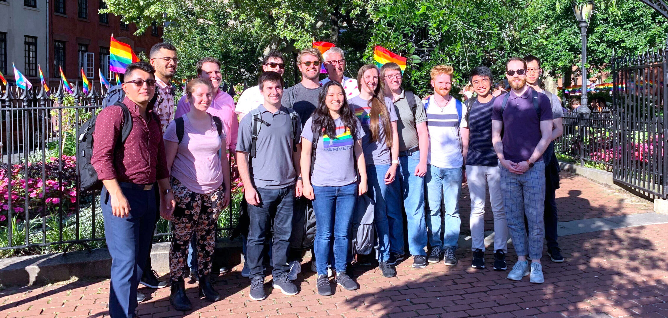 Pariveda employees gather in a park in front of trees wearing PRIDE shirts and holding rainbow flags