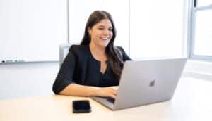 Pariveda employee sitting at a table with a laptop and a phone smiling in the Chicago office