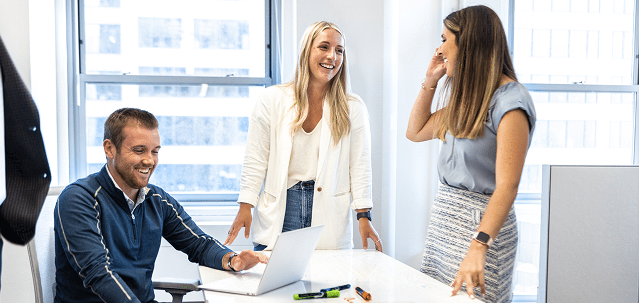 Three Pariveda team members gathered around a whiteboard table working together and talking to each other in the Chicago office