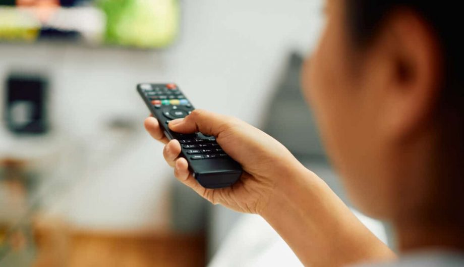Close-up of woman watching Tv and changing channels with remote controller at home