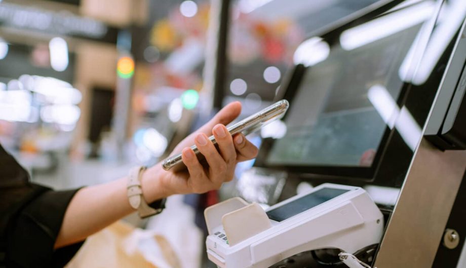 a close up shot of a woman using the self-checkout and paying with her mobile phone at a retail store